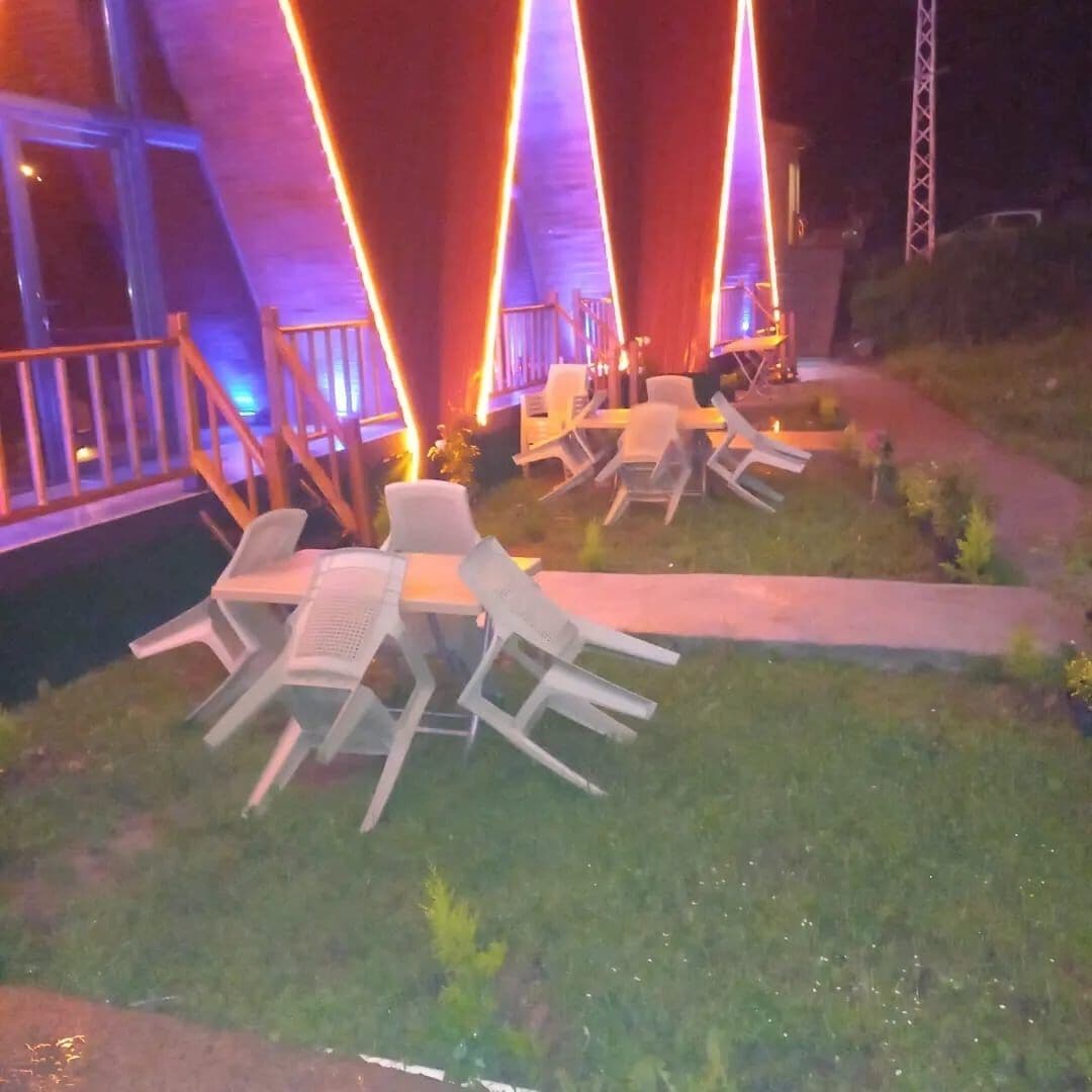 An outdoor seating area with tables and chairs, a pathway, and a building with illuminated vertical structures.