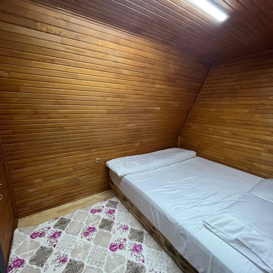 Pequeña habitación con cama individual, paneles de madera en las paredes y una alfombra estampada en el suelo.