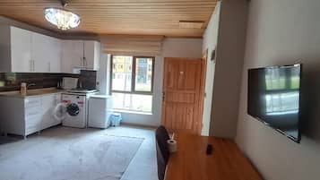 Ein geräumiger Wohnbereich mit einem Holzessttisch, einem an der Wand befestigten Fernseher und einer Küche mit modernen Geräten.