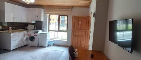 A spacious living area with a wooden dining table, a TV mounted on the wall, and a kitchen with modern appliances.