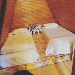 Um quarto pequeno e triangular de madeira, com duas camas, cada uma com roupa de cama branca.