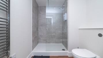 Une salle de bain moderne avec une douche à parois de verre, des toilettes blanches et un porte-serviettes.