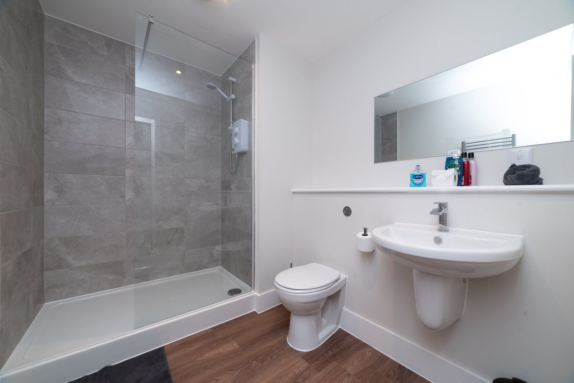 Een moderne badkamer met een glazen douchecabine, een witte wastafel en een toilet.