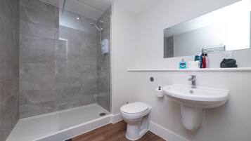 Een moderne badkamer met een glazen douchecabine, een witte wastafel en een toilet.