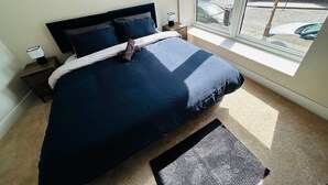 A bedroom with a bed, a nightstand, a window, and a painting on the wall. - Central 1BR Apartment in Hull’s Historic Old Town (Kingston upon Hull)