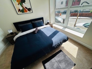 Quarto com cama, mesa de cabeceira, janela e um quadro na parede.