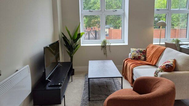 A living room with a sofa, a coffee table, a TV, a plant, and a window with a view of trees and buildings. - Central 1BR Apartment in Hull’s Historic Old Town (Kingston upon Hull)