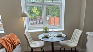 A dining area with a round table, two chairs, a potted plant, and a window with a view of a brick building and trees. - Central 1BR Apartment in Hull’s Historic Old Town (Kingston upon Hull)