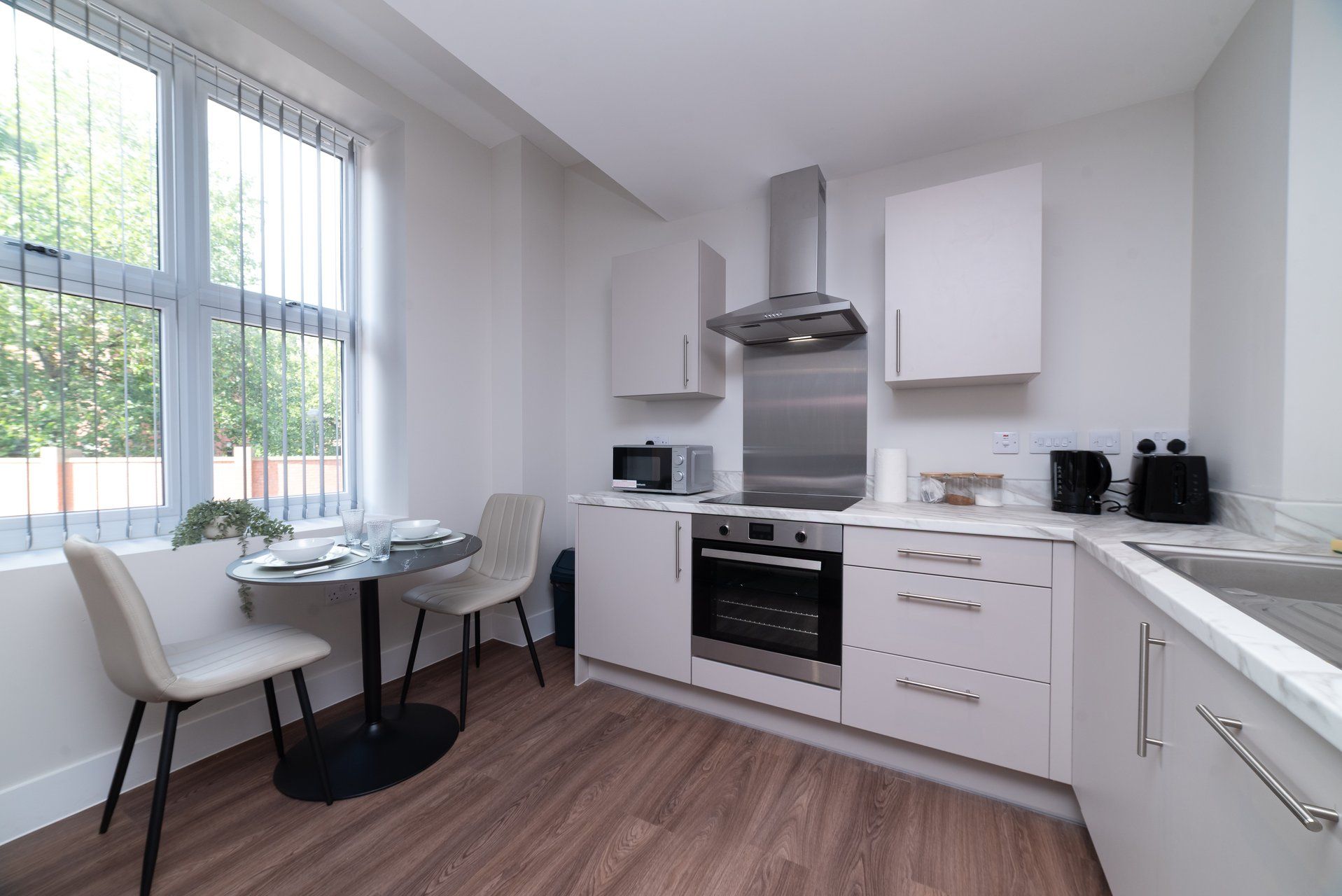 A modern kitchen with white cabinetry, a built-in oven, a microwave, and a stainless steel range hood.