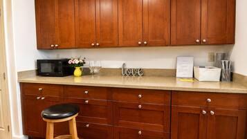 A kitchen with wooden cabinets, a microwave, a vase with flowers, and a stool.