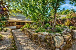 A house with a stone retaining wall, a gravel pathway, and a variety of plants and trees. - Family-Friendly 4BR/3BA N Seattle,Private Yard, AC (Seattle)