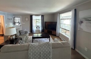 A living room with a sofa, coffee table, TV, and a large window with curtains.