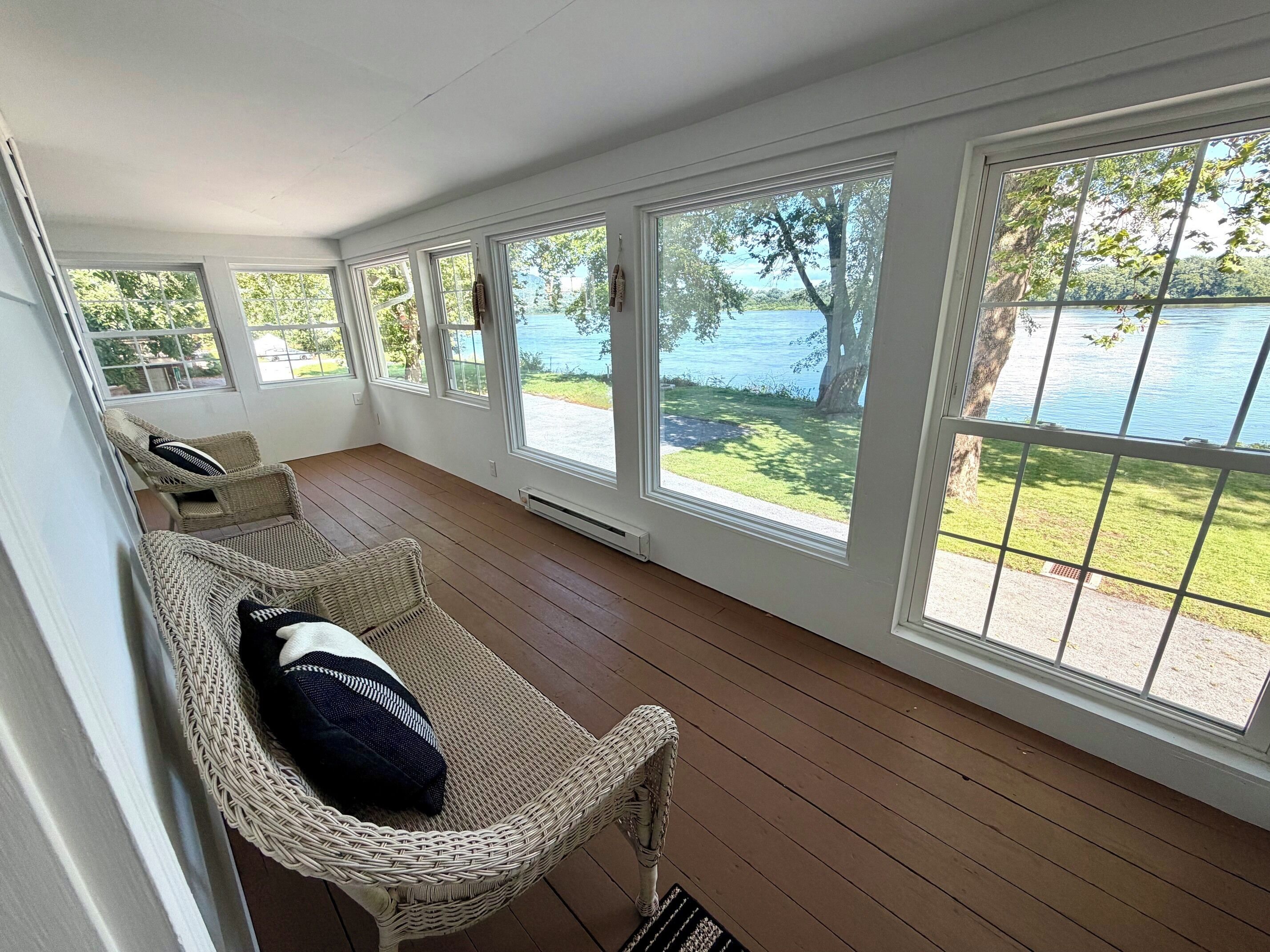 A room with a view of a lake, wicker furniture, and large windows.