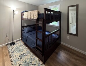 Een slaapkamer met stapelbed, een kamerbreed tapijt met dessin, een staande lamp en een raam met uitzicht.