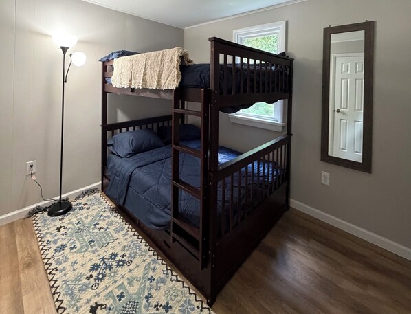 A bunk bed room with a patterned rug, a standing lamp, and a window with a view.