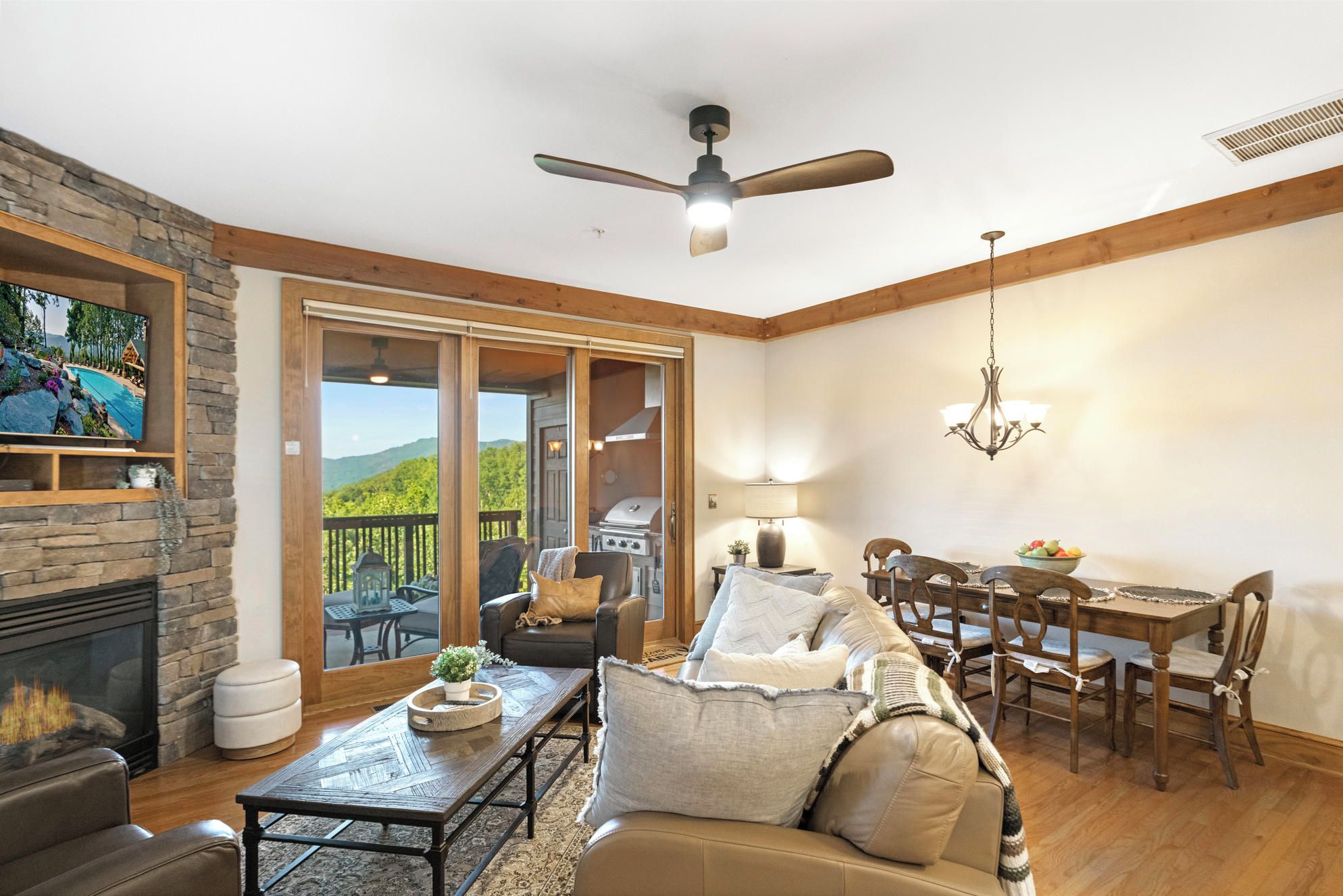 A cozy living room with a fireplace, a television, a dining area with a chandelier, and a view of the outdoors.