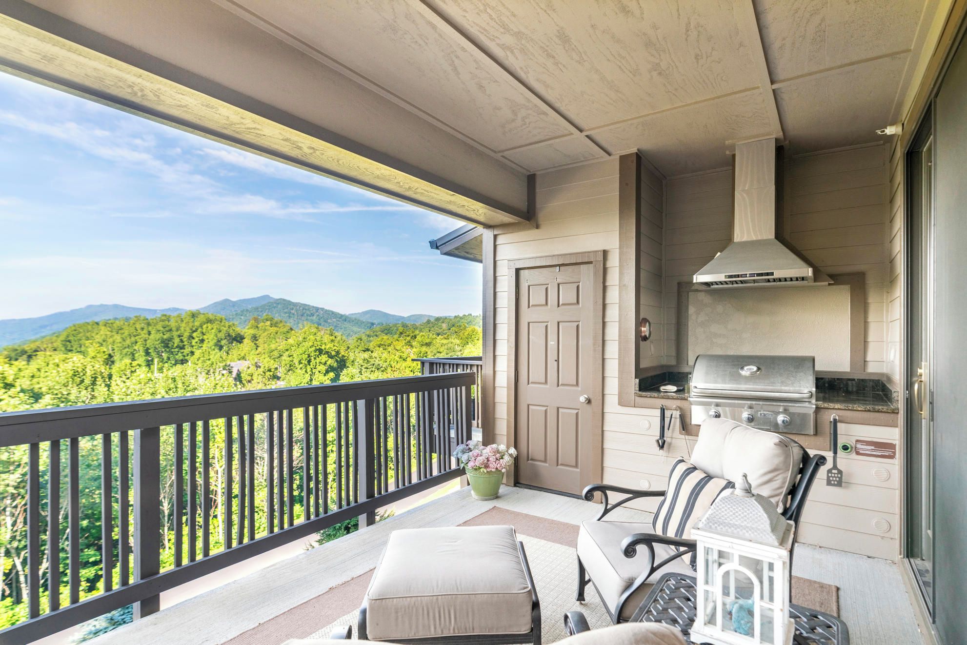 A balcony with a view of a forested mountain range, a barbecue grill, and a door.