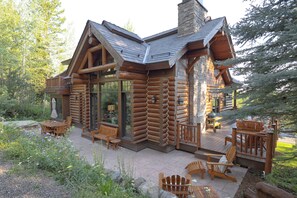 Eine Blockhütte mit einer Terrasse, Sitzgelegenheiten im Freien und einem Steinkamin.