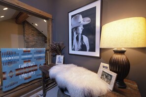 Quarto com fotografia a preto e branco emoldurada na parede, luminária sobre uma mesa, tapete estampado e um banco de madeira.