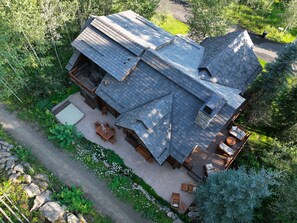 Eine rustikale Holzhütte mit geneigtem Dach, einer Terrasse mit Gartenmöbeln und einer umliegenden Naturlandschaft.