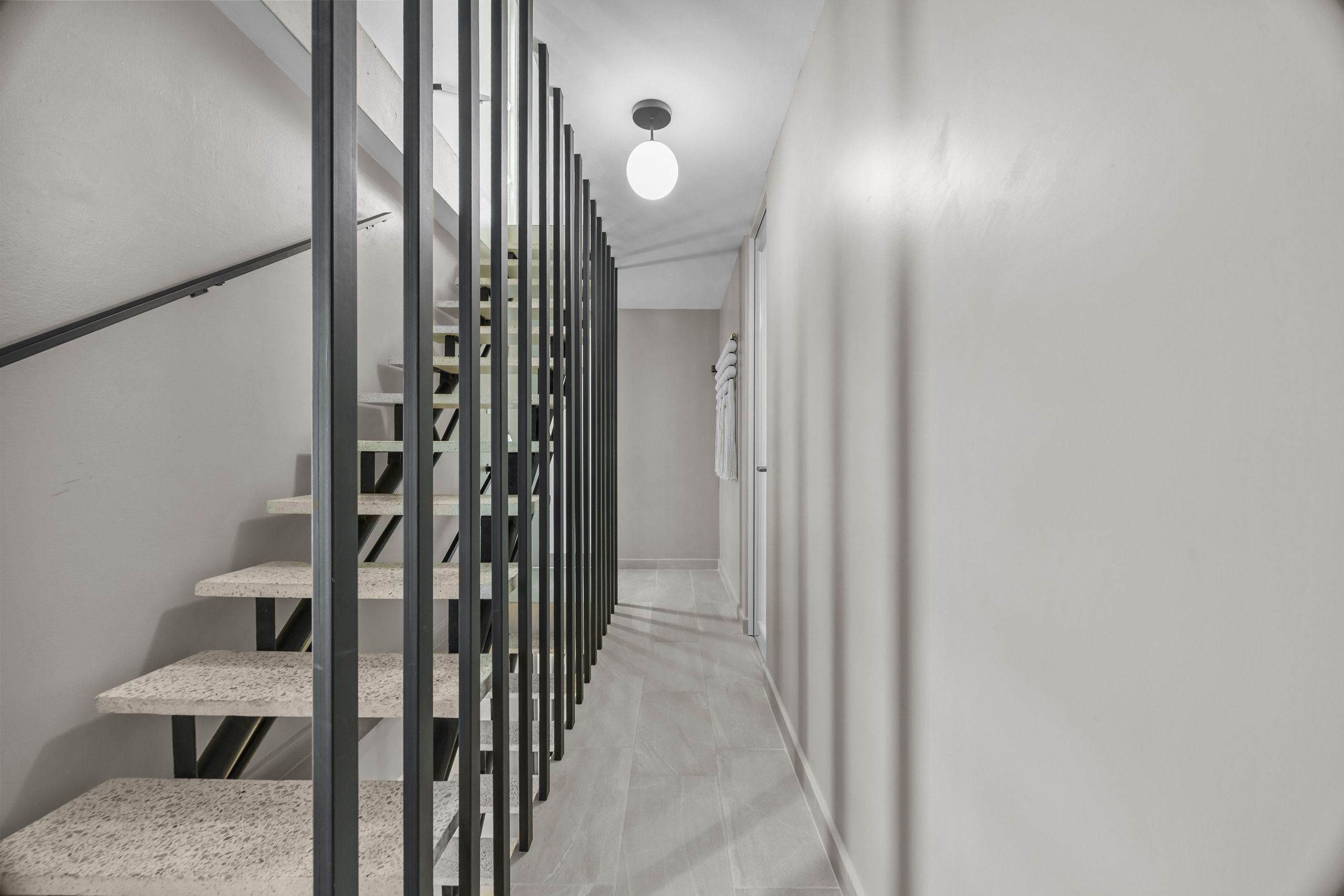 Una escalera moderna con barandilla de metal, que conduce a un rellano con una lámpara.