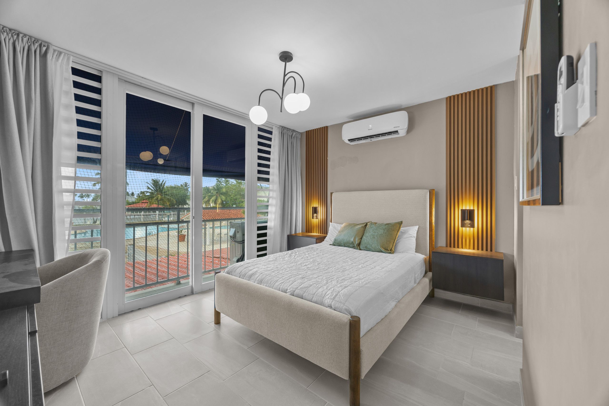 Quarto de hotel com cama, escrivaninha, cadeira e varanda com piscina, além de ar condicionado.