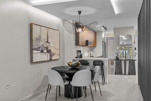 A modern kitchen with a dining area, featuring a round table with chairs, a pendant light, and a large abstract painting on the wall.