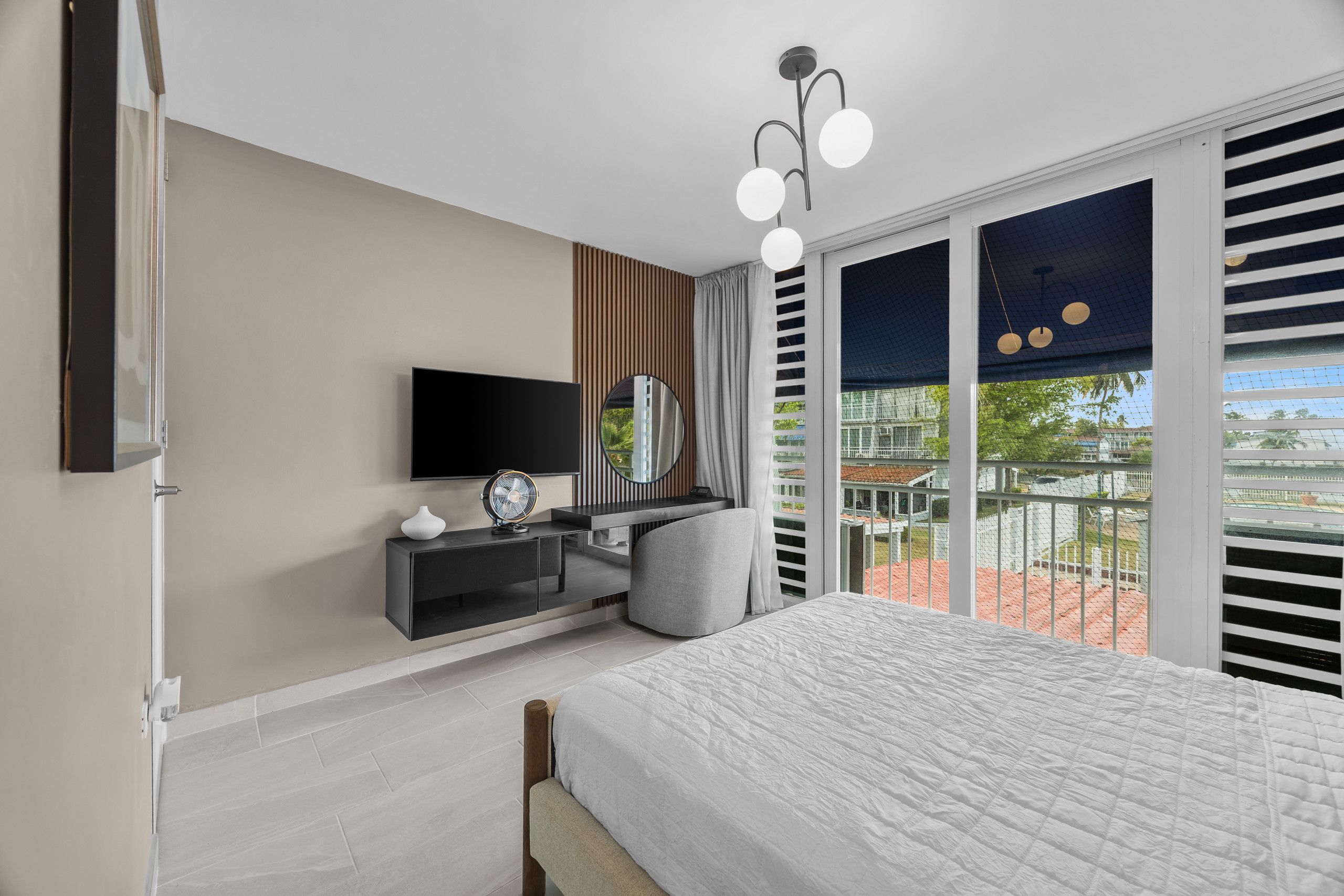 Un dormitorio moderno con una cama, televisor, escritorio y un amplio ventanal con vistas.