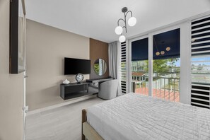 A modern bedroom with a bed, a TV, a desk, and a large window with a view.