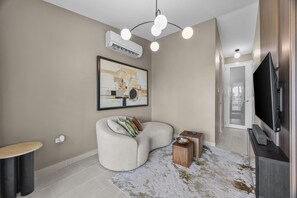 Een moderne woonkamer met een hoekbank, een flatscreen televisie, een wandairconditioner en een moderne lamp.