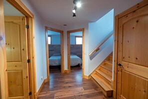 Un pasillo con puertas de madera, una escalera y una cama al fondo.