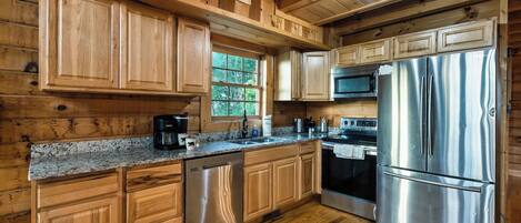 L’intérieur d’un chalet en bois comprend une cuisine équipée d’un réfrigérateur en acier inoxydable, d’un four à micro-ondes, d’une cuisinière et de meubles de rangement en bois.