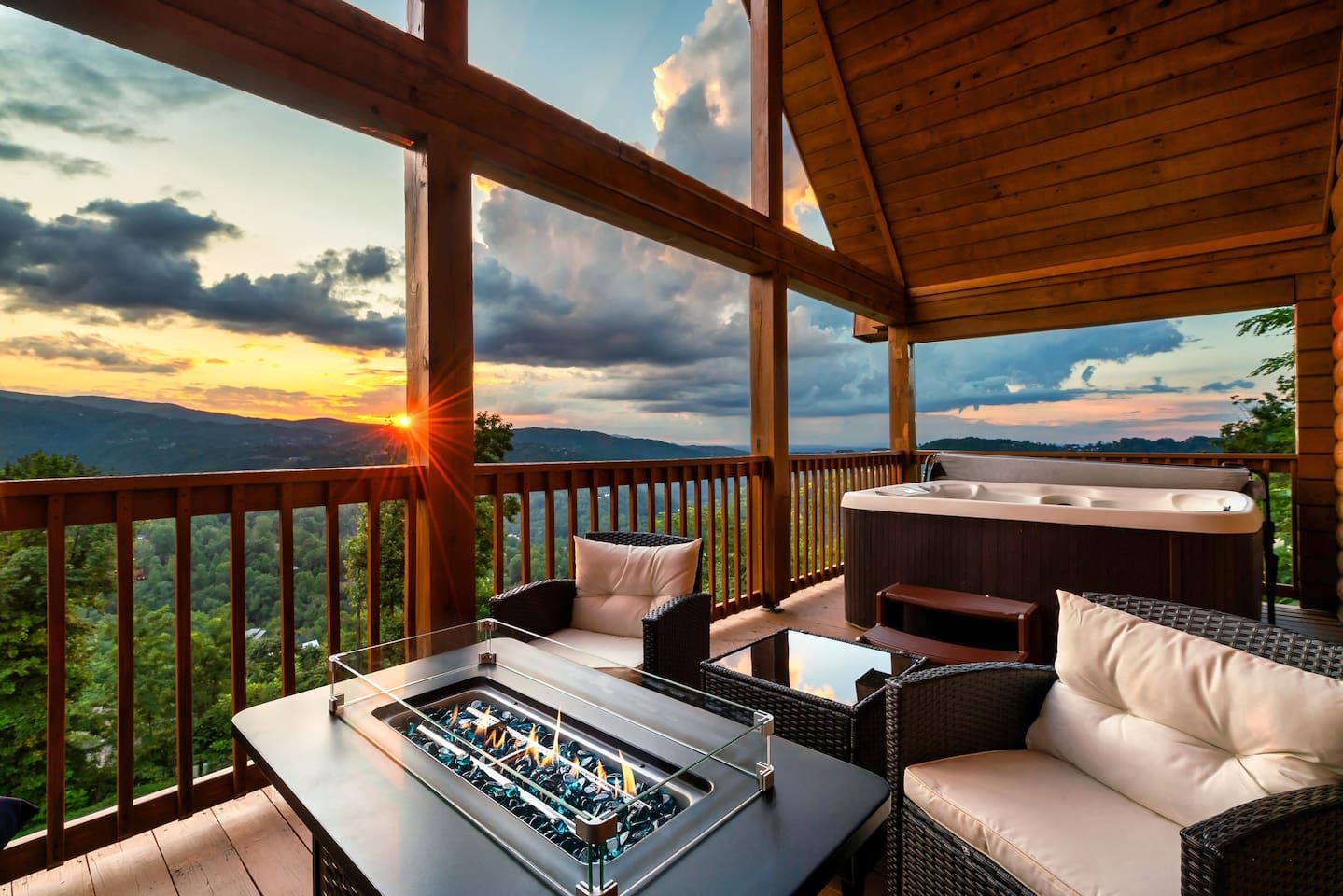 Una terraza de madera con un jacuzzi, mobiliario exterior y vistas a las montañas.