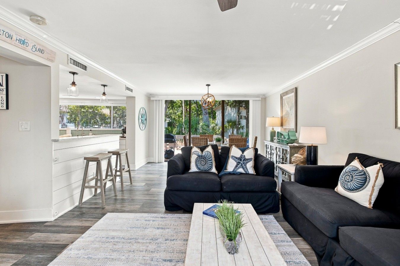 A modern living room with a black sofa set, a coffee table with a plant, and a view to the outside.