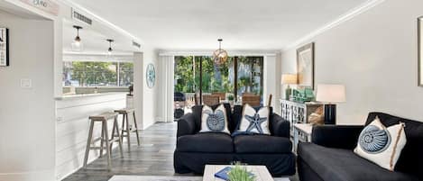A modern living room with a black sofa set, a coffee table with a plant, and a view to the outside.