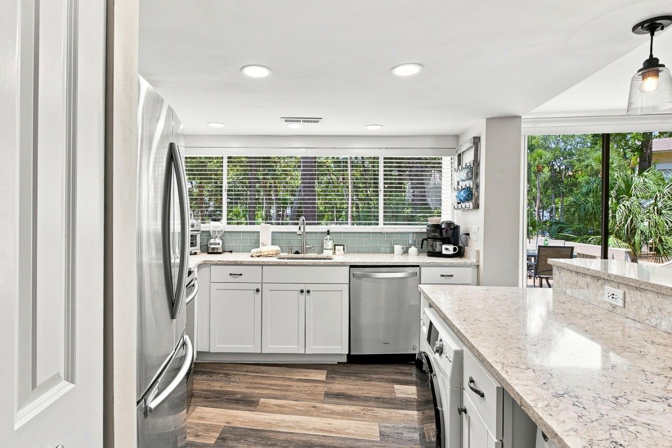 A modern kitchen with white cabinets, a stainless steel dishwasher, and a herringbone wood floor.
