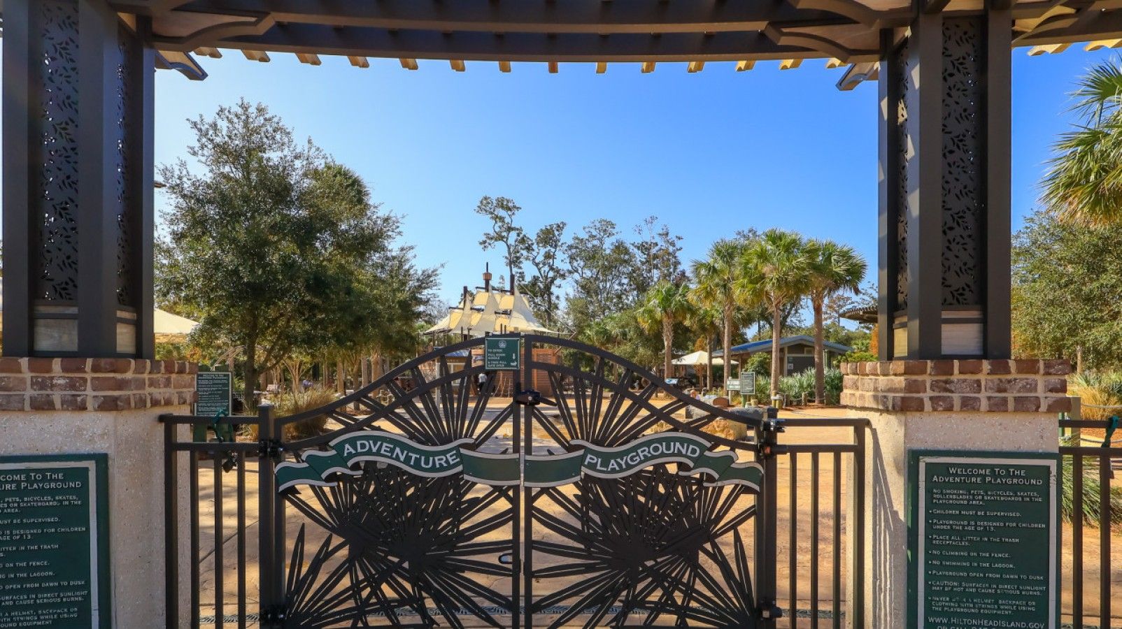 A gated entrance to an outdoor playground area with a sign indicating 'Adventure Playground' and 'Playground.'