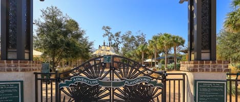 A gated entrance to an outdoor playground area with a sign indicating 'Adventure Playground' and 'Playground.'