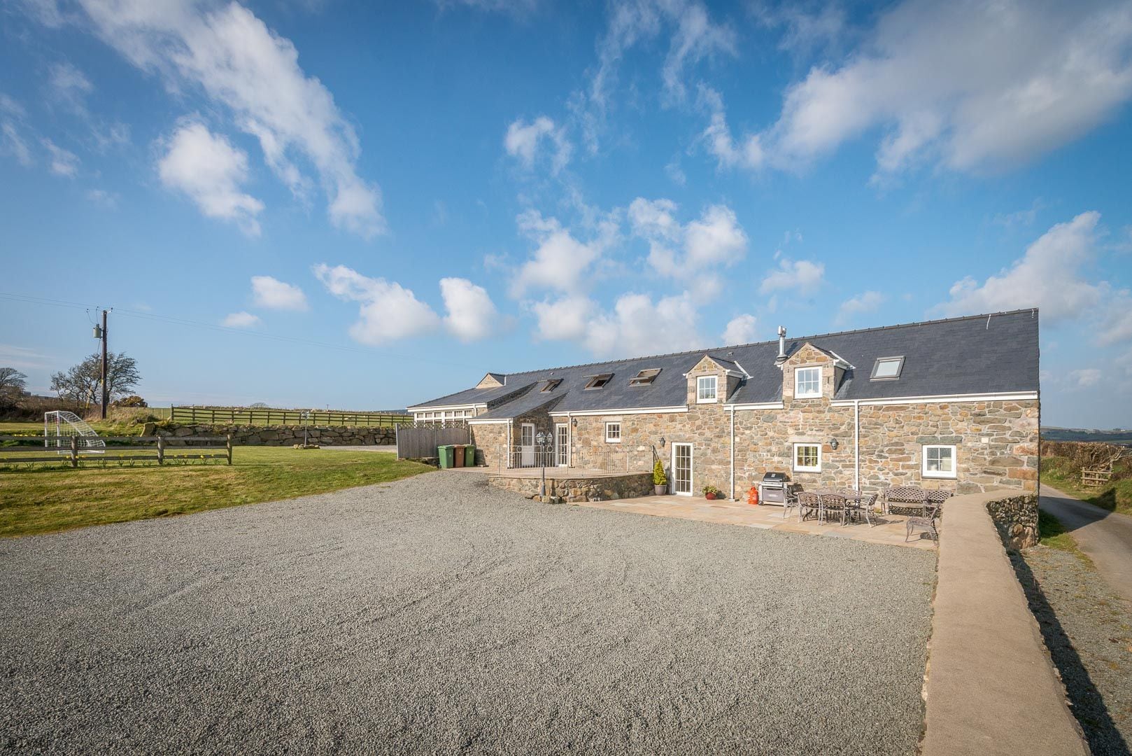 A stone building with a gravel driveway, a fenced area, and a clear sky.