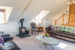 A cozy living room with a fireplace, a leather sofa, a dining table, and a staircase. - Large Converted Barn Near Abersoch | Gadlas-Sarn (Pwllheli)
