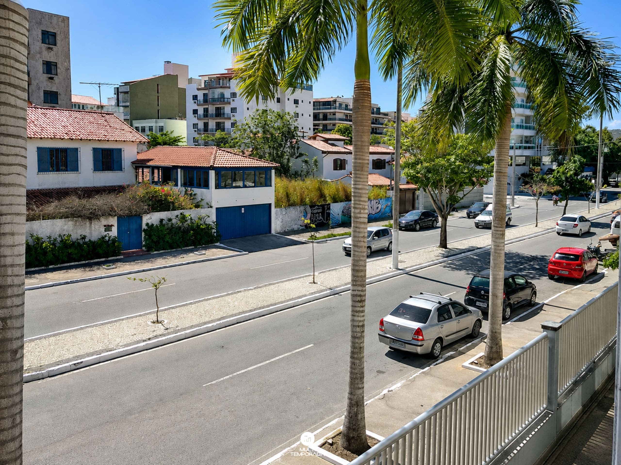 Straßenansicht mit Gebäuden, Autos und Palmen.