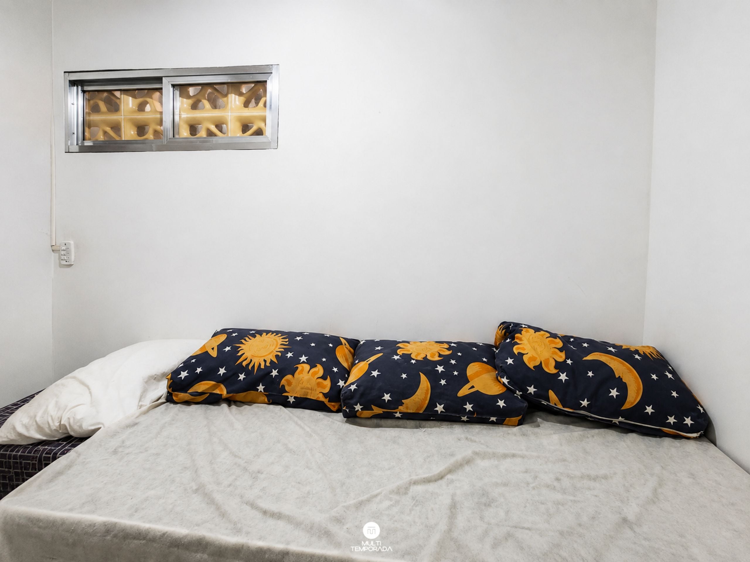 A bed with a white pillow and two pillows with a star and moon pattern.