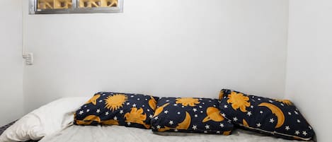 Una cama con un almohadón blanco y dos almohadas con estampado de estrella y luna.