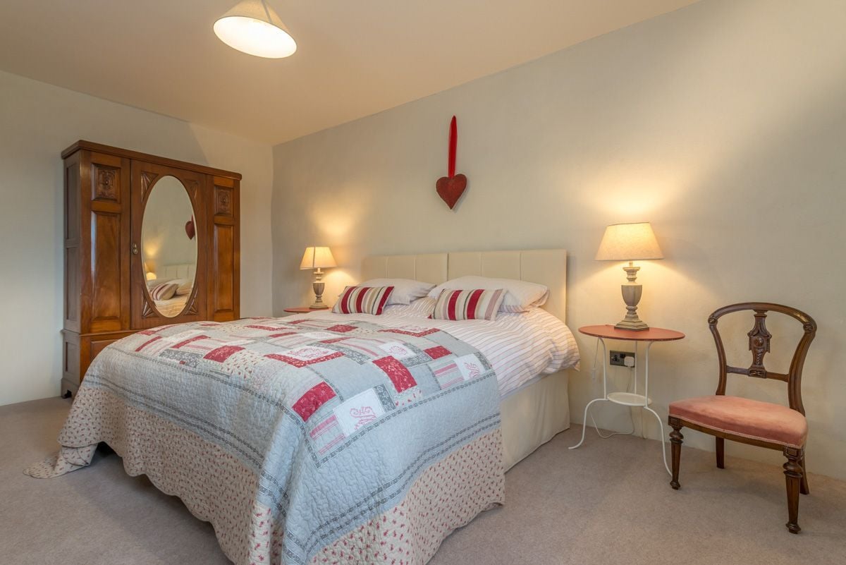 A bedroom with a bed, a wooden wardrobe, two bedside lamps, a red heart decoration, and a chair.