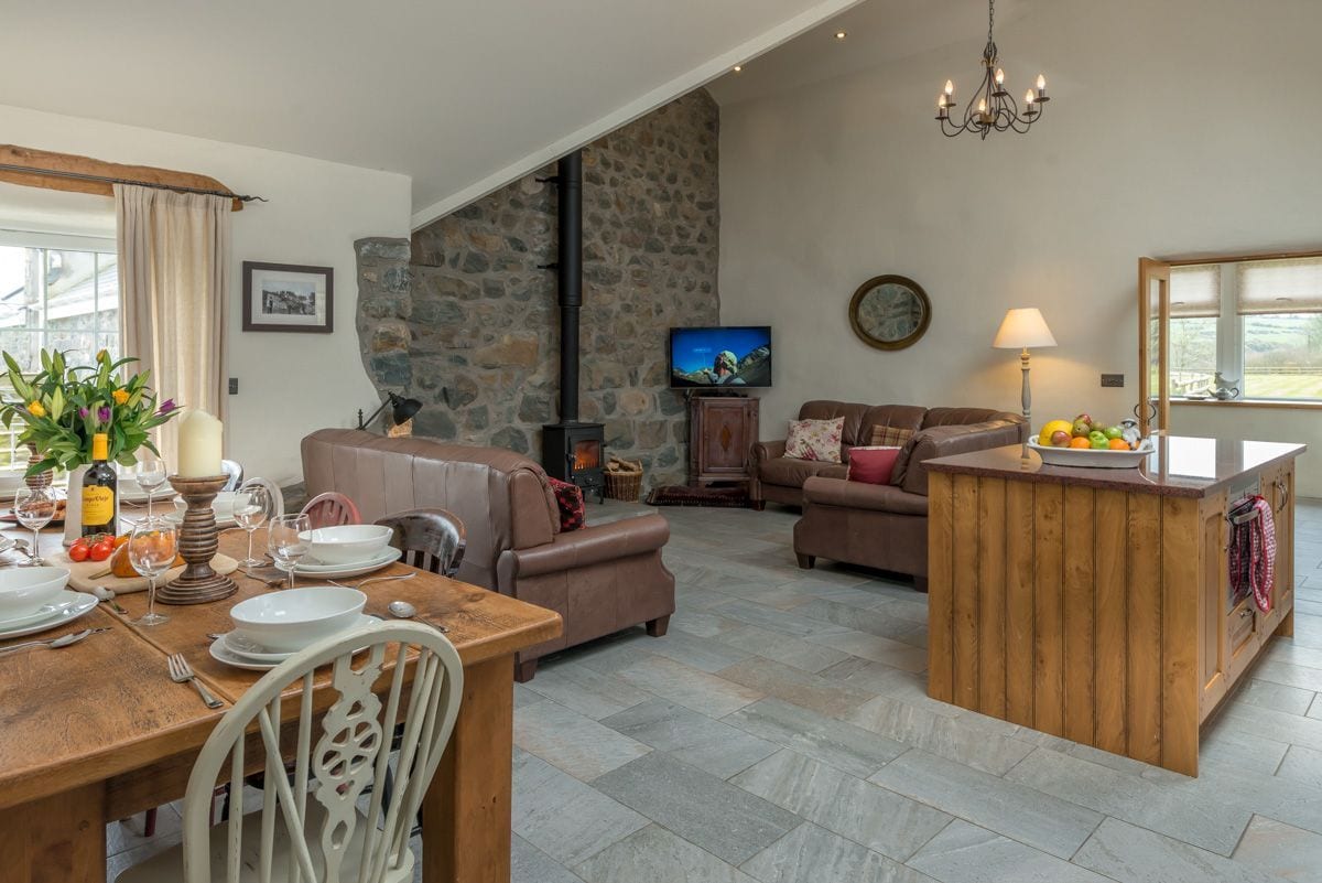 Uma sala de estar acolhedora com parede de pedra, lareira, televisão e área de jantar com mesa e cadeiras de madeira.