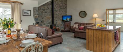 Uma sala de estar acolhedora com parede de pedra, lareira, televisão e área de jantar com mesa e cadeiras de madeira.