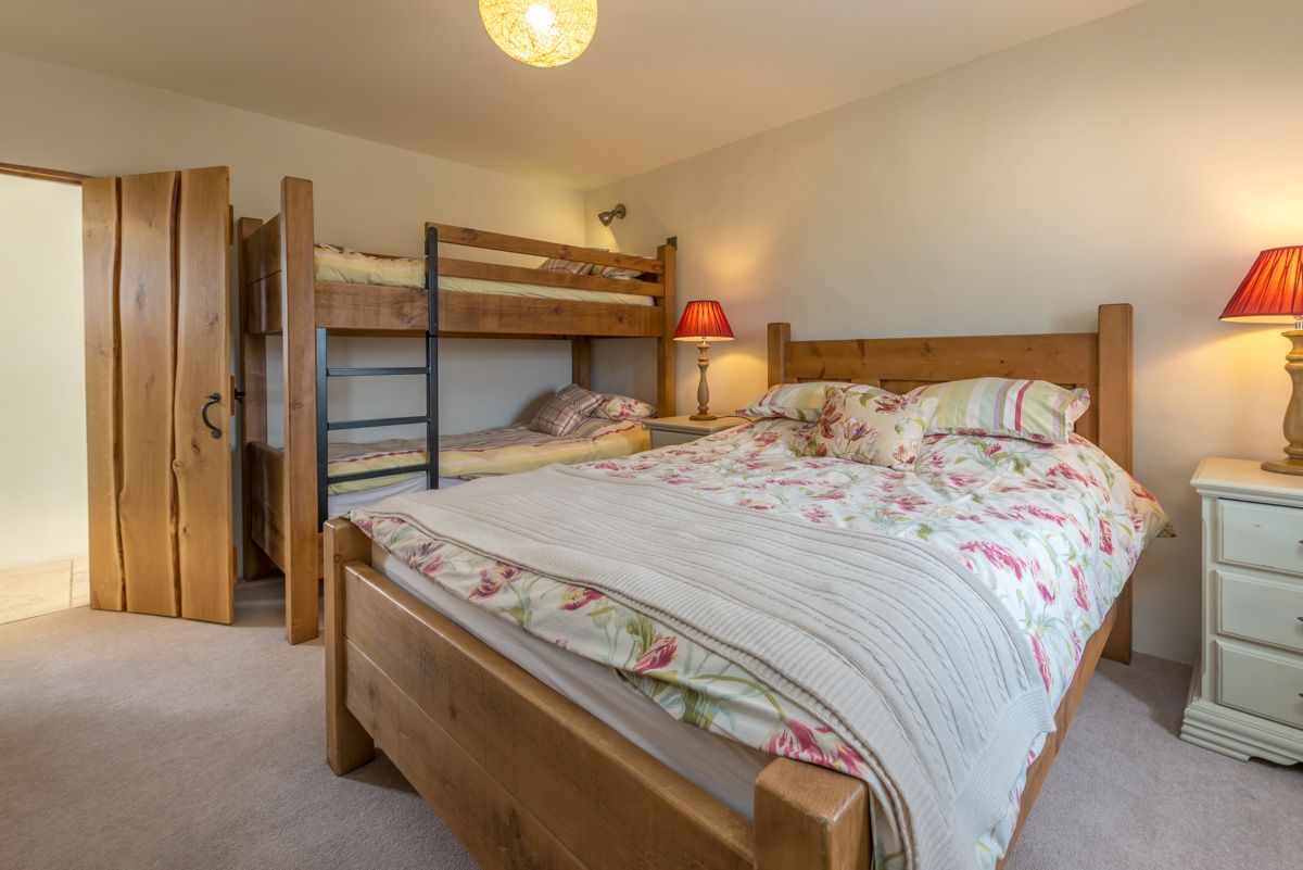 A bedroom with a bunk bed, a single bed, a bedside table with a lamp, and a wardrobe.