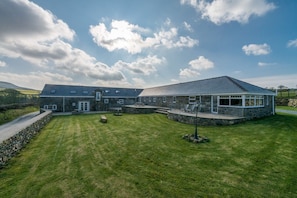 A large stone building with a flat roof, a covered patio area, and a well-maintained lawn. - Self Catering For Large Groups on The Llŷn Peninsula | Mynachdy-Sarn (Pwllheli)