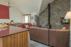 A cozy living area with a stone fireplace, a wooden island with fruit, and a comfortable seating arrangement. - Self Catering For Large Groups on The Llŷn Peninsula | Mynachdy-Sarn (Pwllheli)