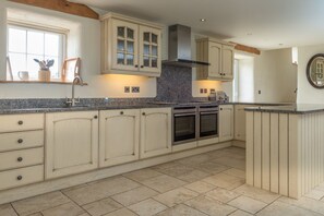 A kitchen with light-colored cabinetry, a granite countertop, a built-in oven, and a window with a view. - Self Catering For Large Groups on The Llŷn Peninsula | Mynachdy-Sarn (Pwllheli)